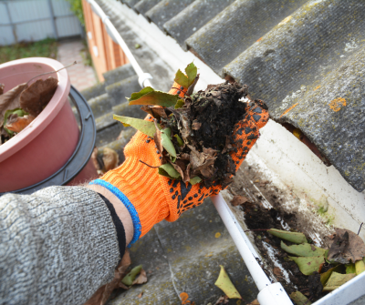 An orange gloved hand removing debris from a gutter to winterize